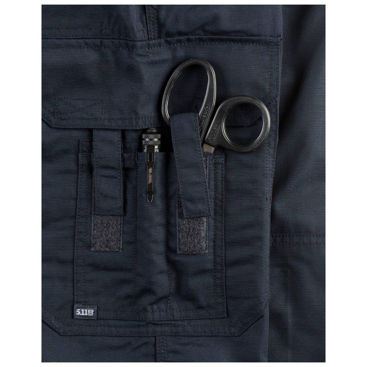 Navy blue tactical jacket with a sheath of scissors in a pocket, featuring the 5.11 logo.